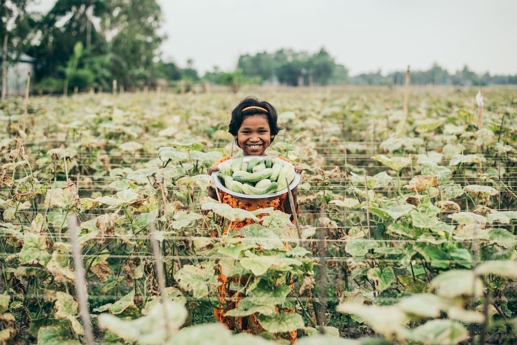 A child standing in a field holding a bowl of vegetables.